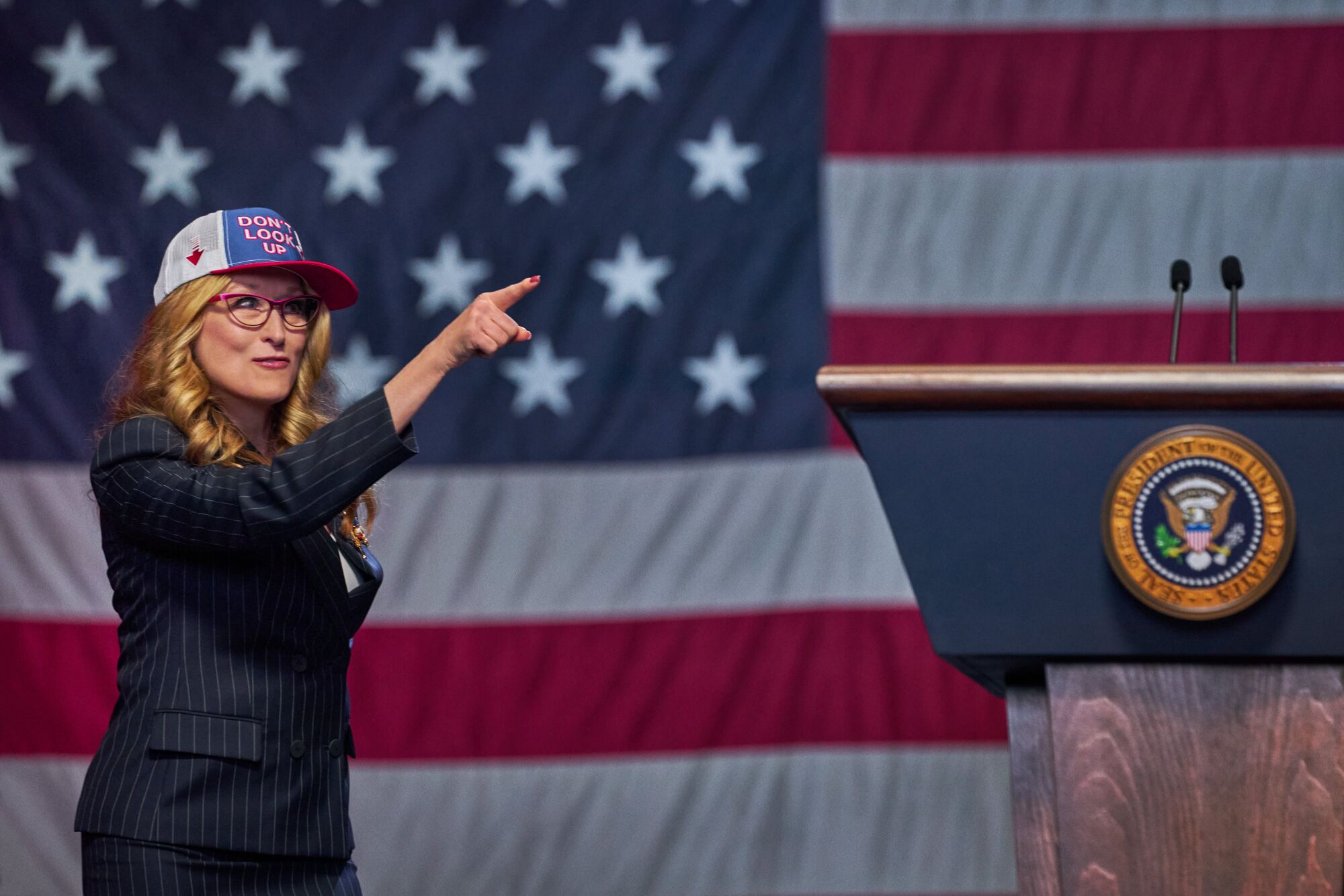 A woman in a hat pointing in front of a giant American flag