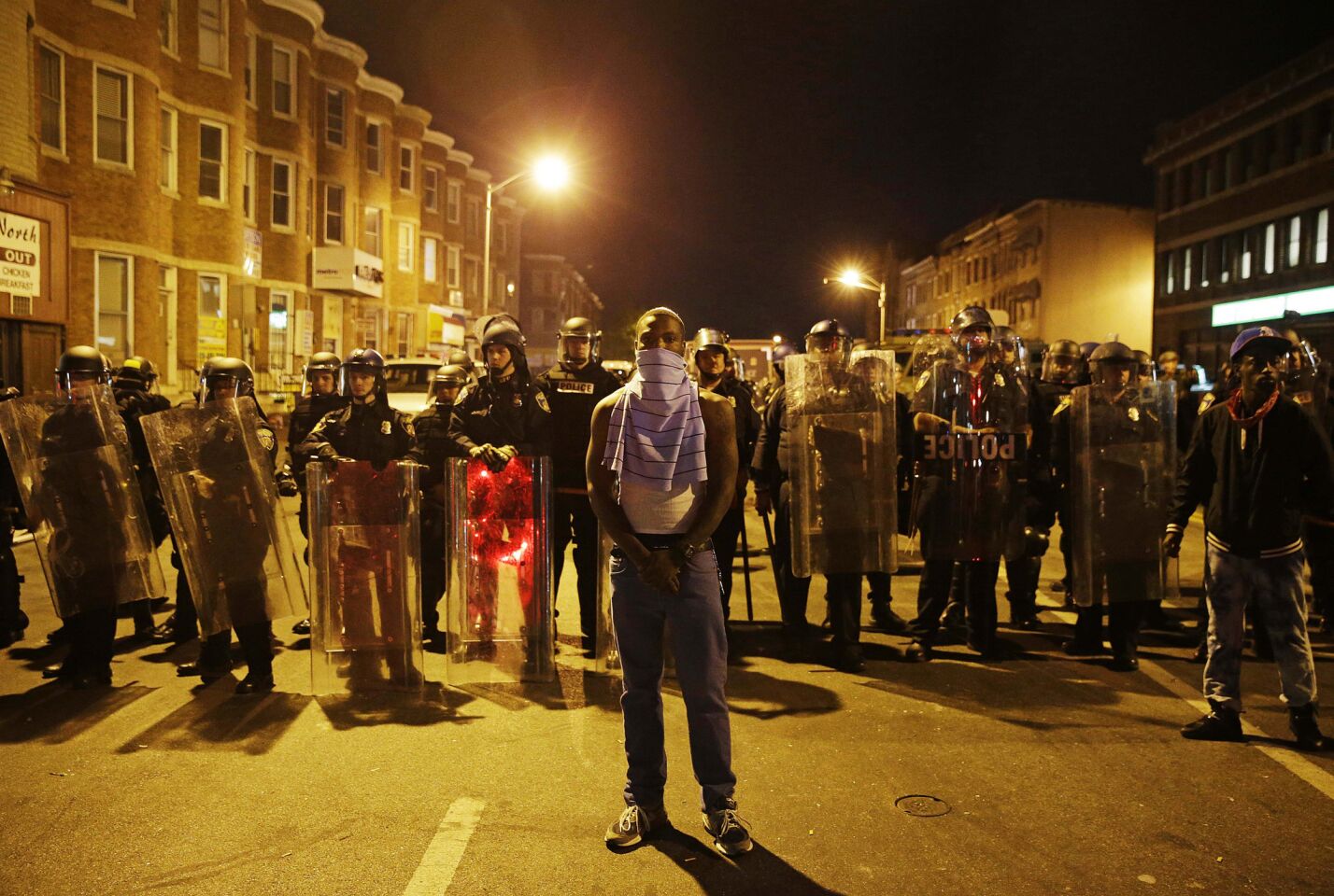 A man stands in front of a line of police officers in riot gear ahead of a 10 p.m. curfew on Tuesday in Baltimore.