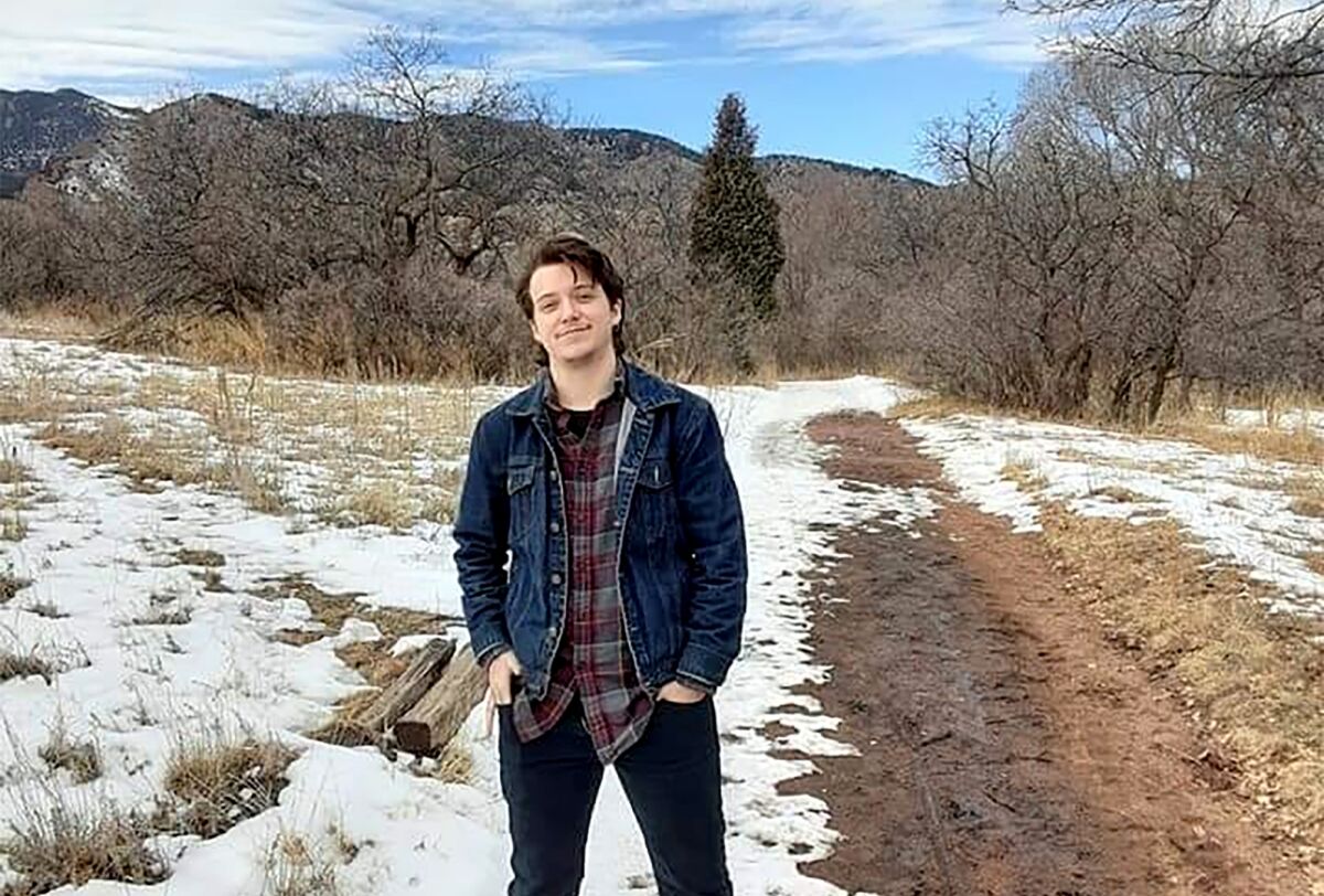 Daniel Aston stands outdoors with a dirt road and snow behind him.