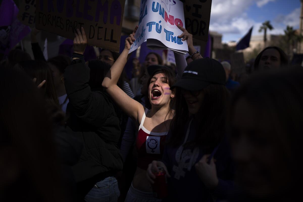 A woman looks up as she holds a sign over her head and yells during a protest march.