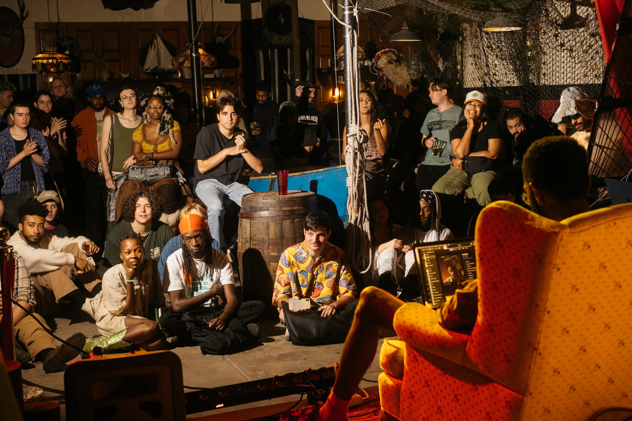 A group of people standing and seated in a room look at someone sitting in an orange chair