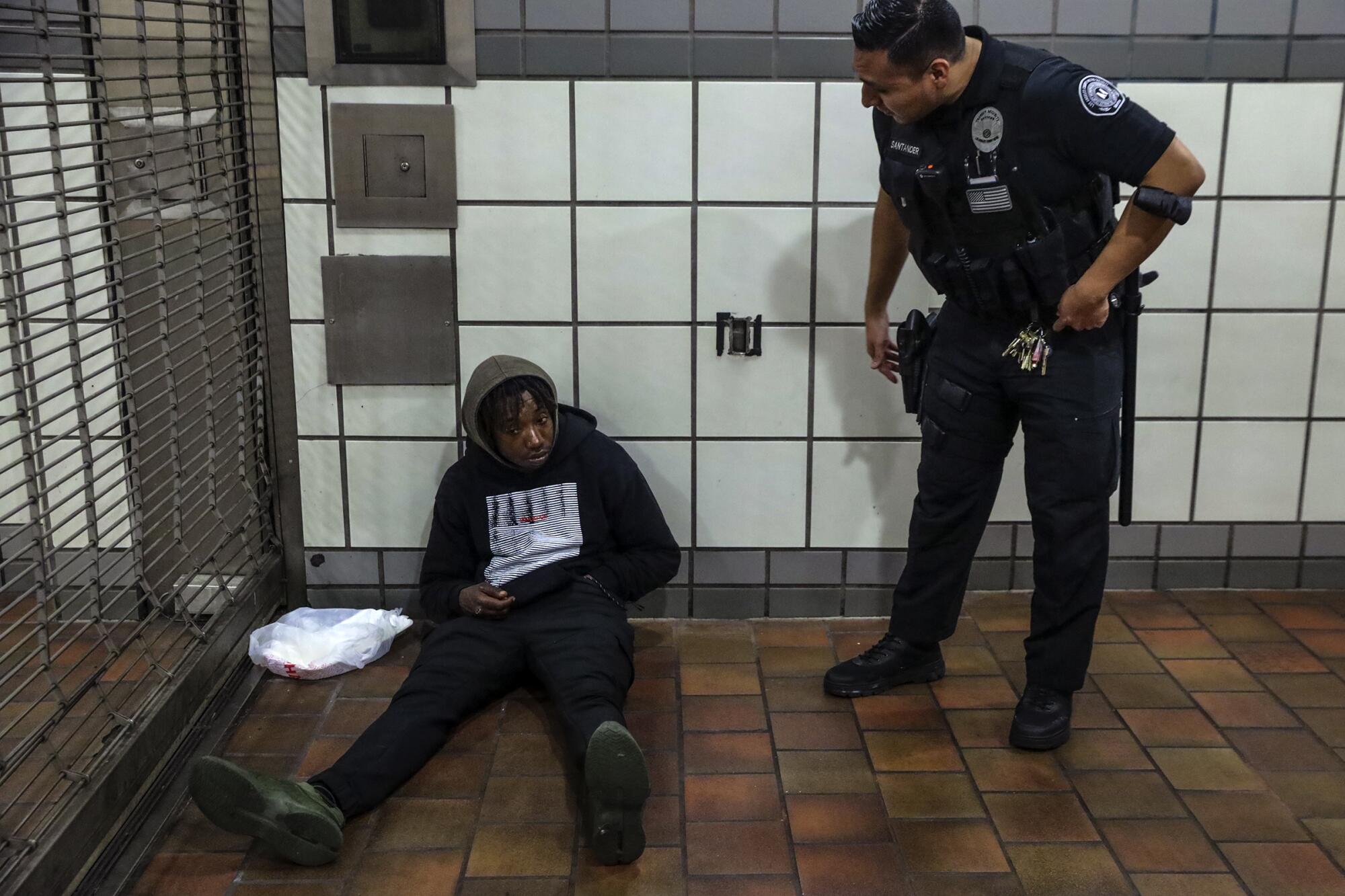 Officer Kevin Santander, right, wakes up a homeless man sleeping in front of the closed gates 