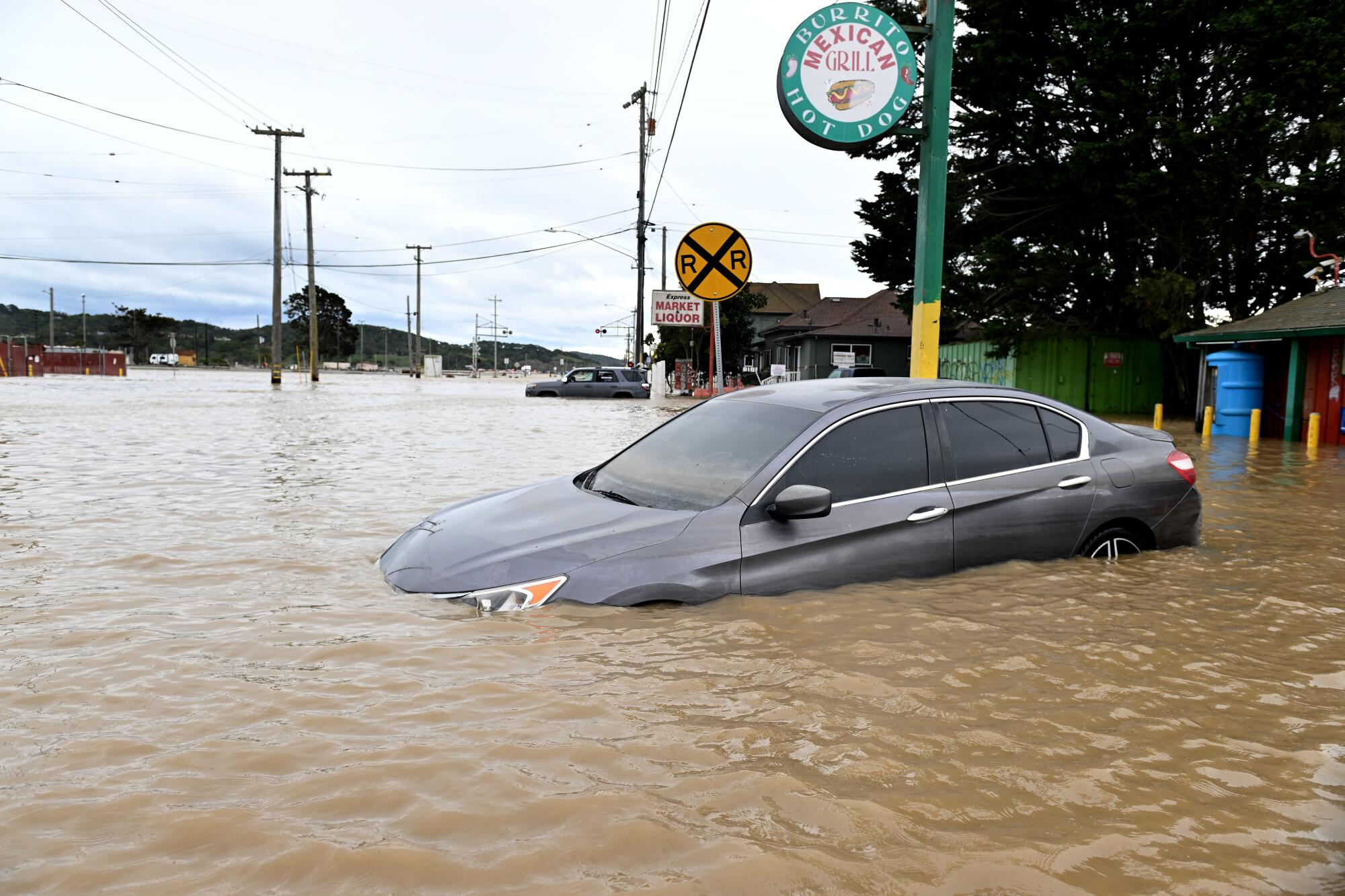 A car sits half submerged in muddy floodwater.