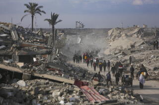 Palestinians walk through heaps of rubble.