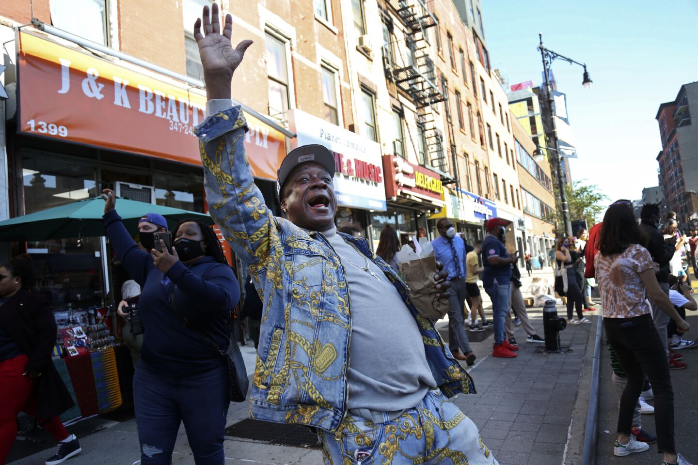 Marcel Cothron sings "Na na na na, hey hey hey goodbye" with a large crowd gathered on Fulton Street in Brooklyn