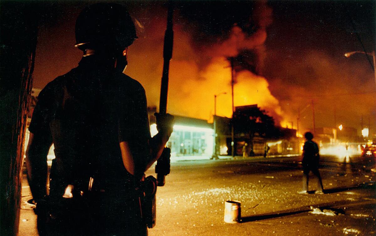 LAPD Officer Delwin Fields guards the intersection at Central and 46th Street as fires burn buildings nearby