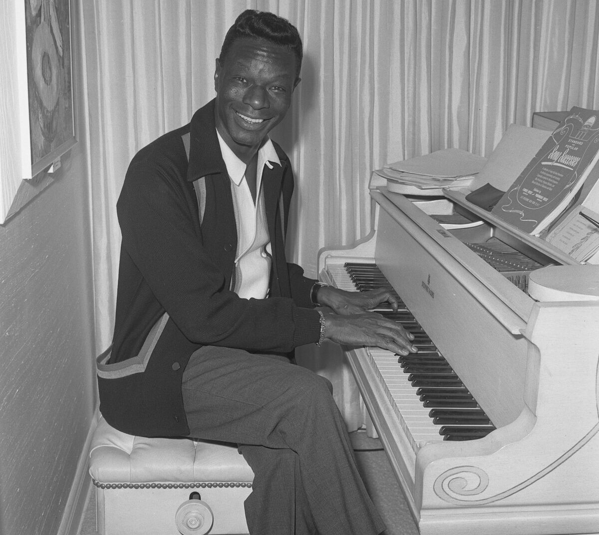 Nat King Cole smiles while seated at a piano.