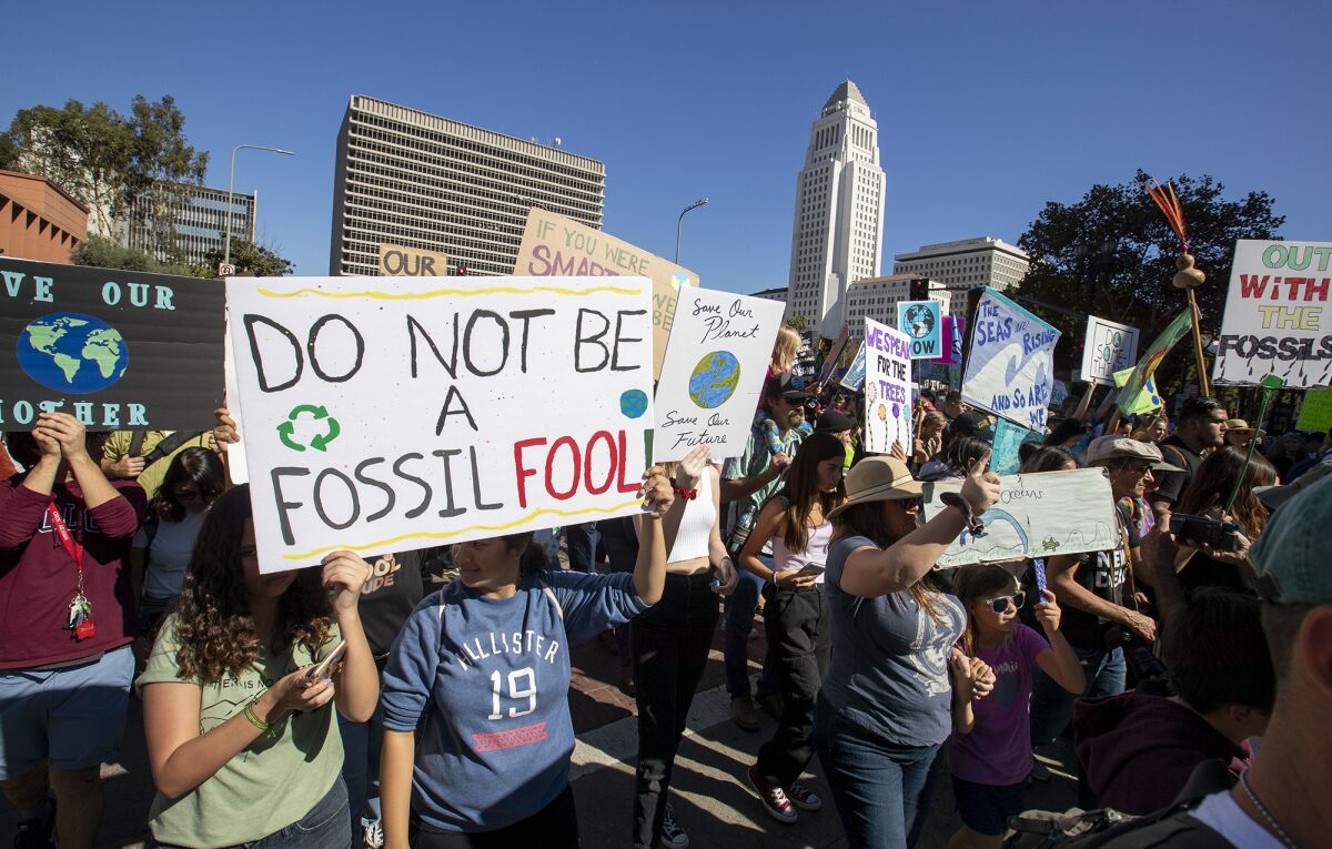 People hold up signs at a protest. One sign says: Do not be a fossil fool