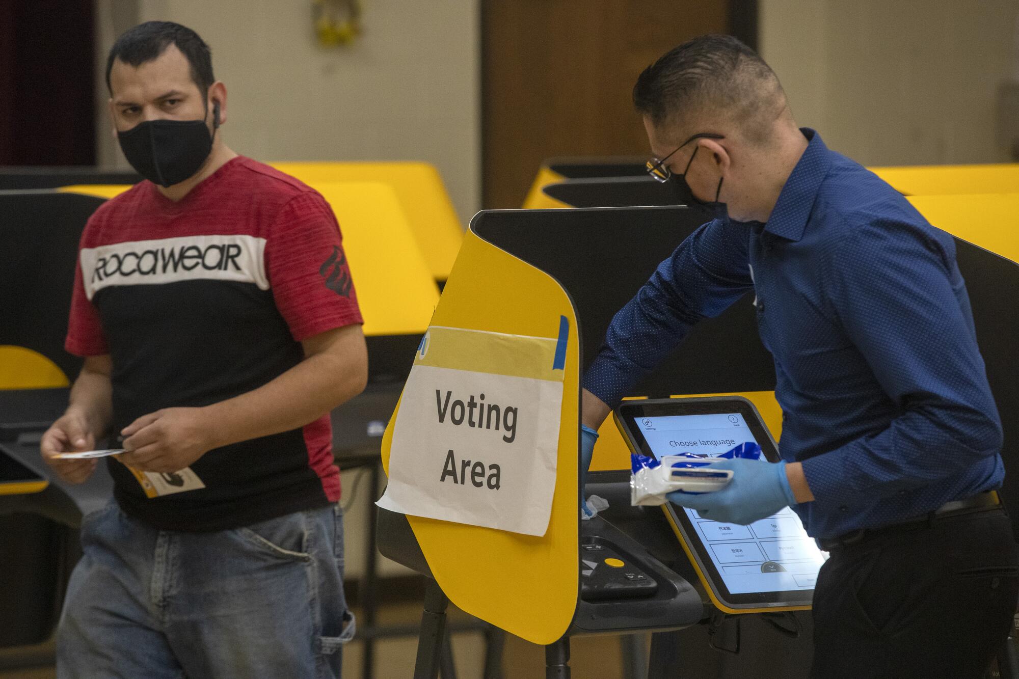 A poll worker, right, sanitizes a voting machine