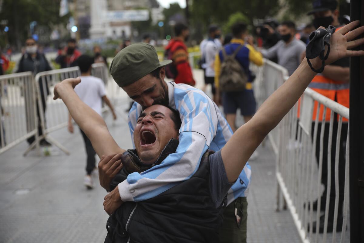 One mourner props up and embraces another man, whose arms are flung wide as he sobs.