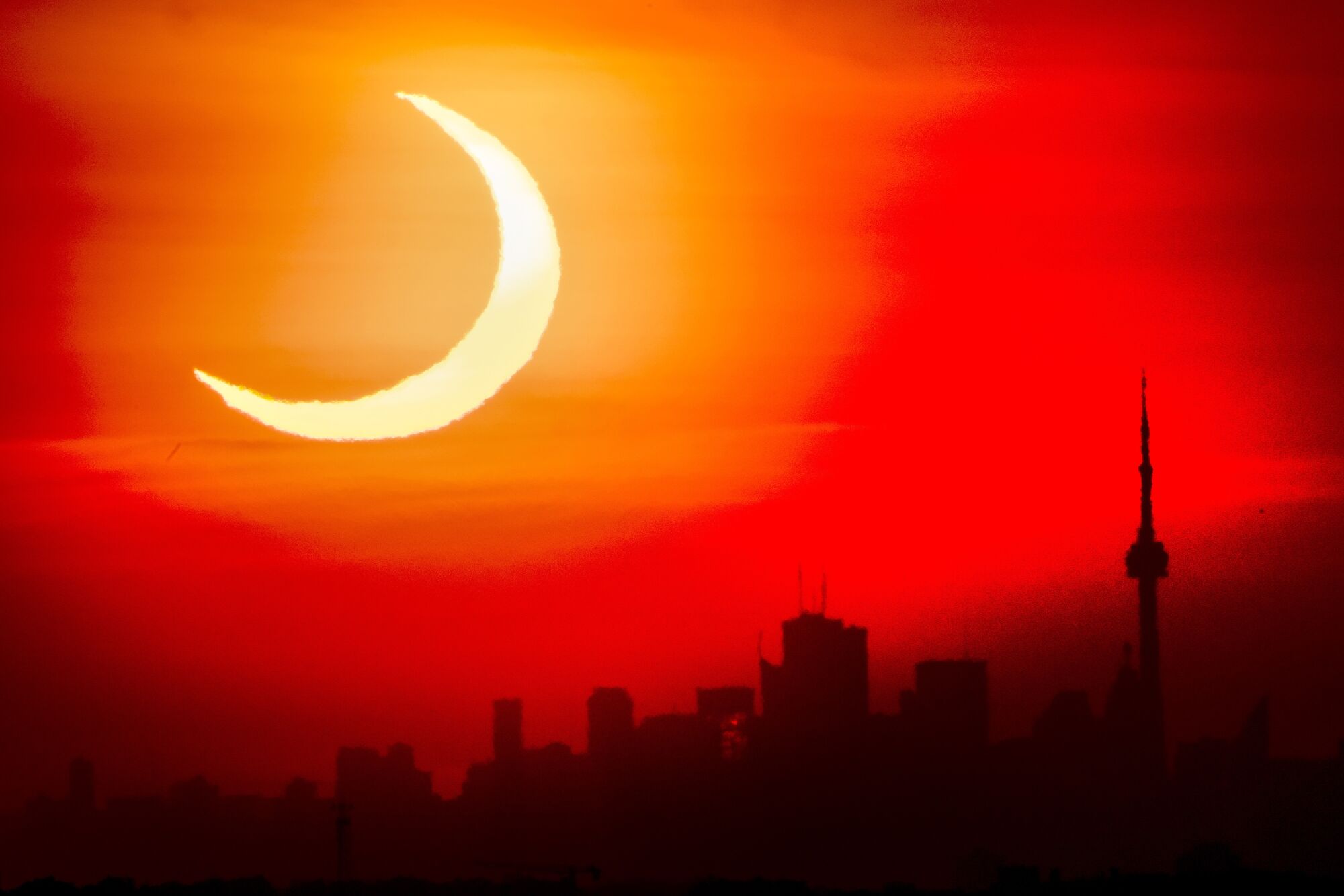 An annular solar eclipse rises over the skyline of Toronto.