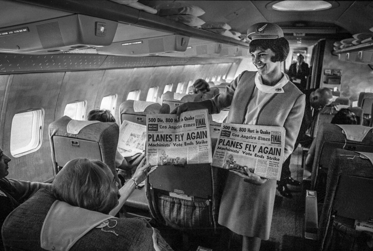 A flight attendant smiles and hands a passenger a newspaper