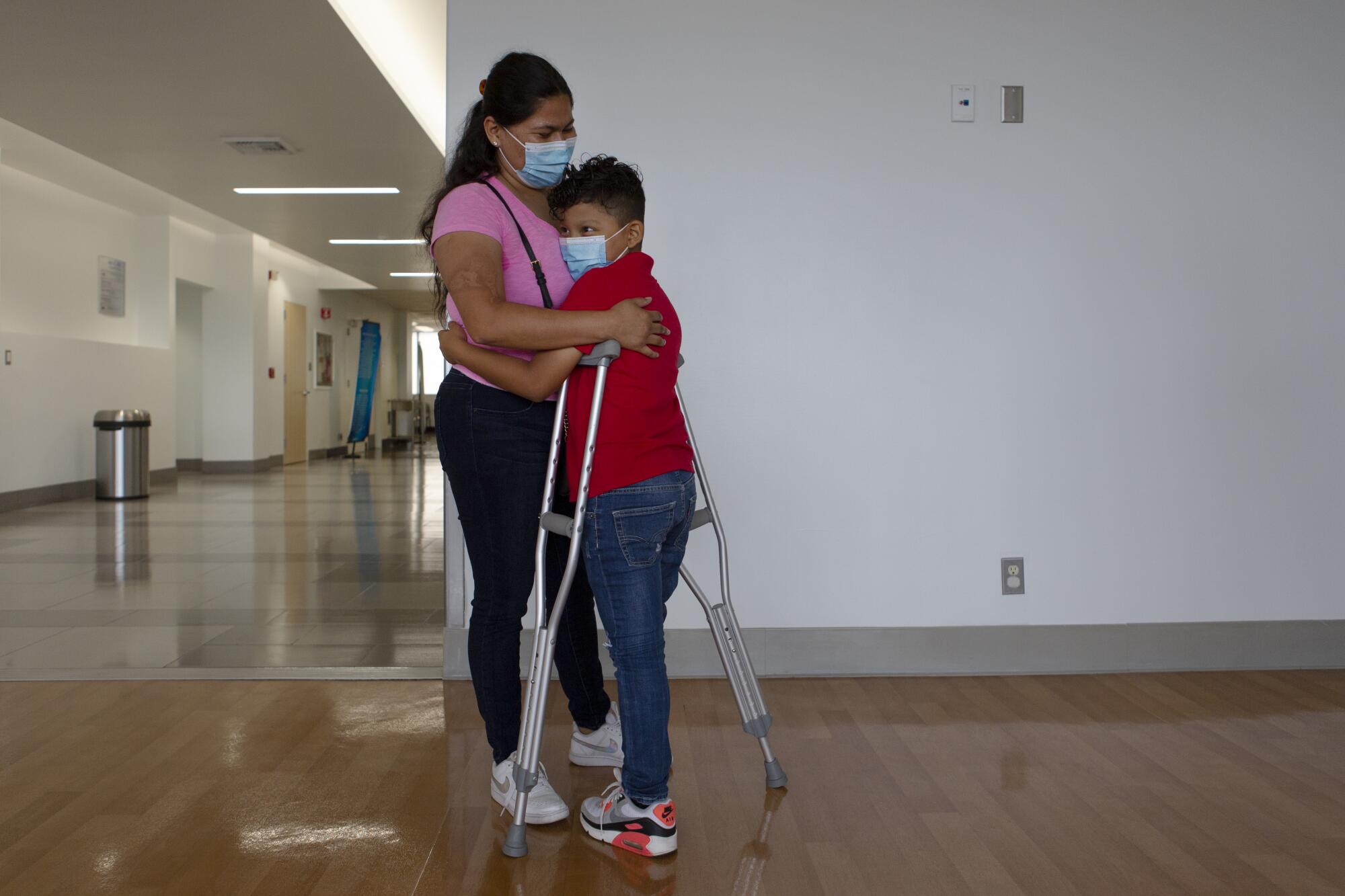 Efrain stands with his crutches and hugs his mother