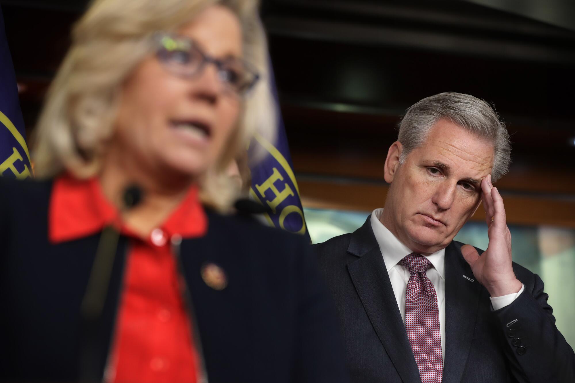 A man puts his hand on his face while a woman speaks.