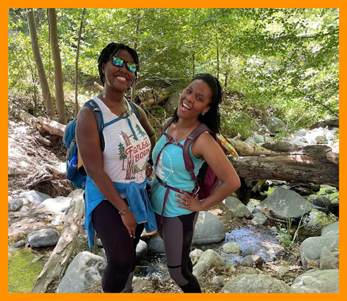 Two Black women, Tiffany Tharpe and Michelle Warren, stand next to each other in front of a rocky forested area.