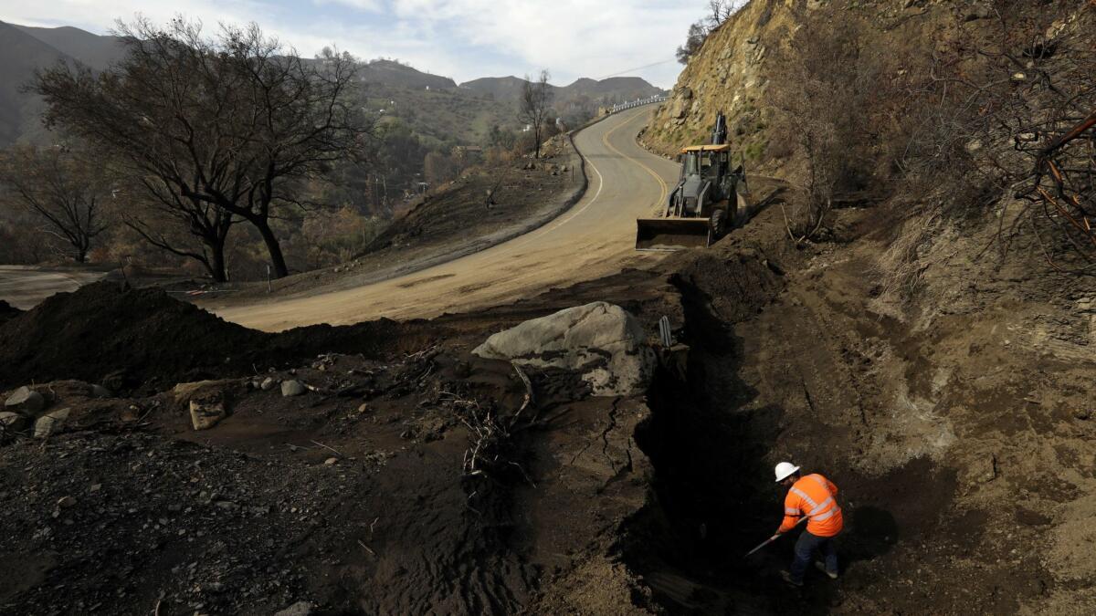 A Caltrans worker digs out dirt from around a storm drain on Decker Canyon, in preparation for the rain expected Saturday.