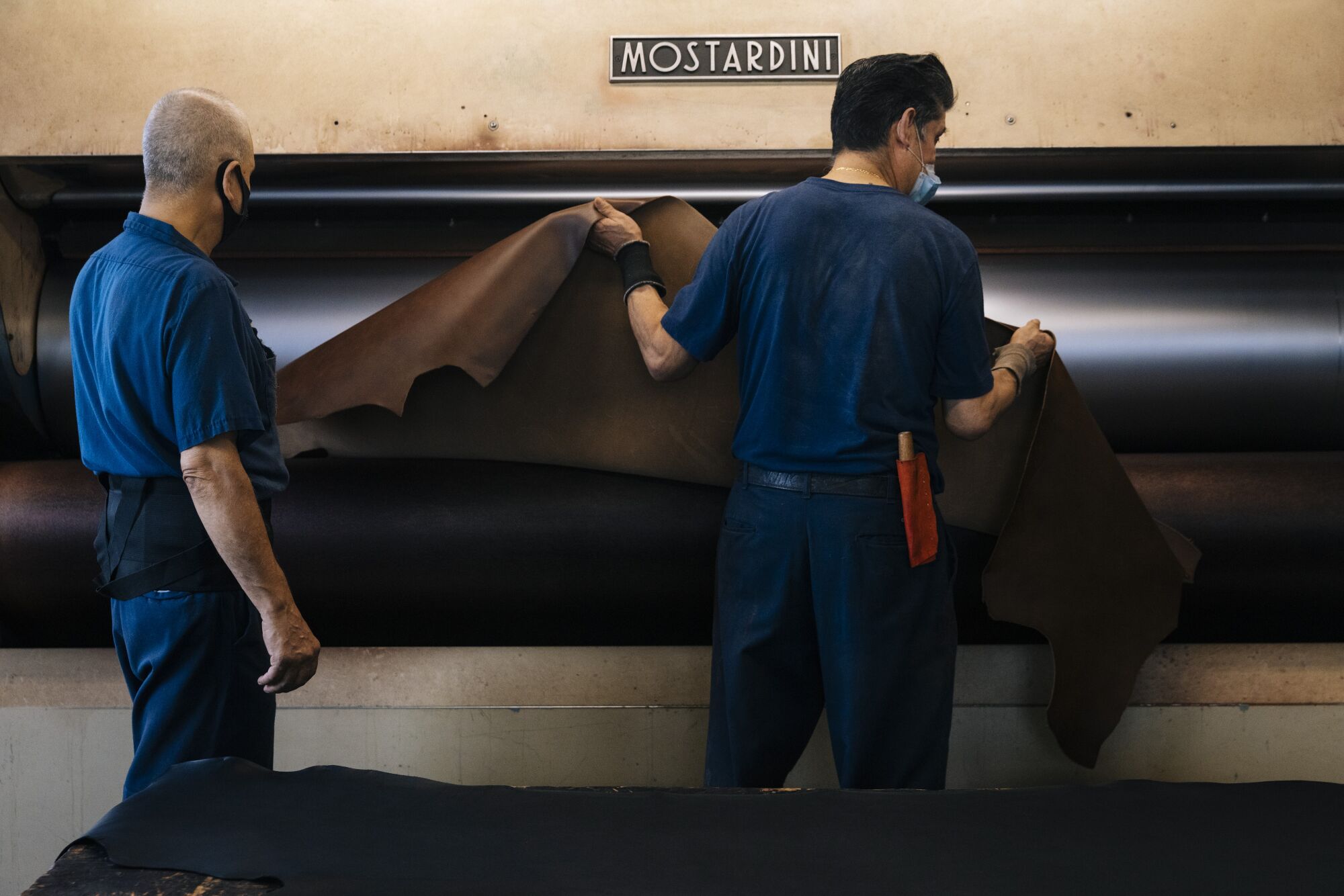 Workers remove a piece of leather from the ironing machine at the Horween Leather Company.
