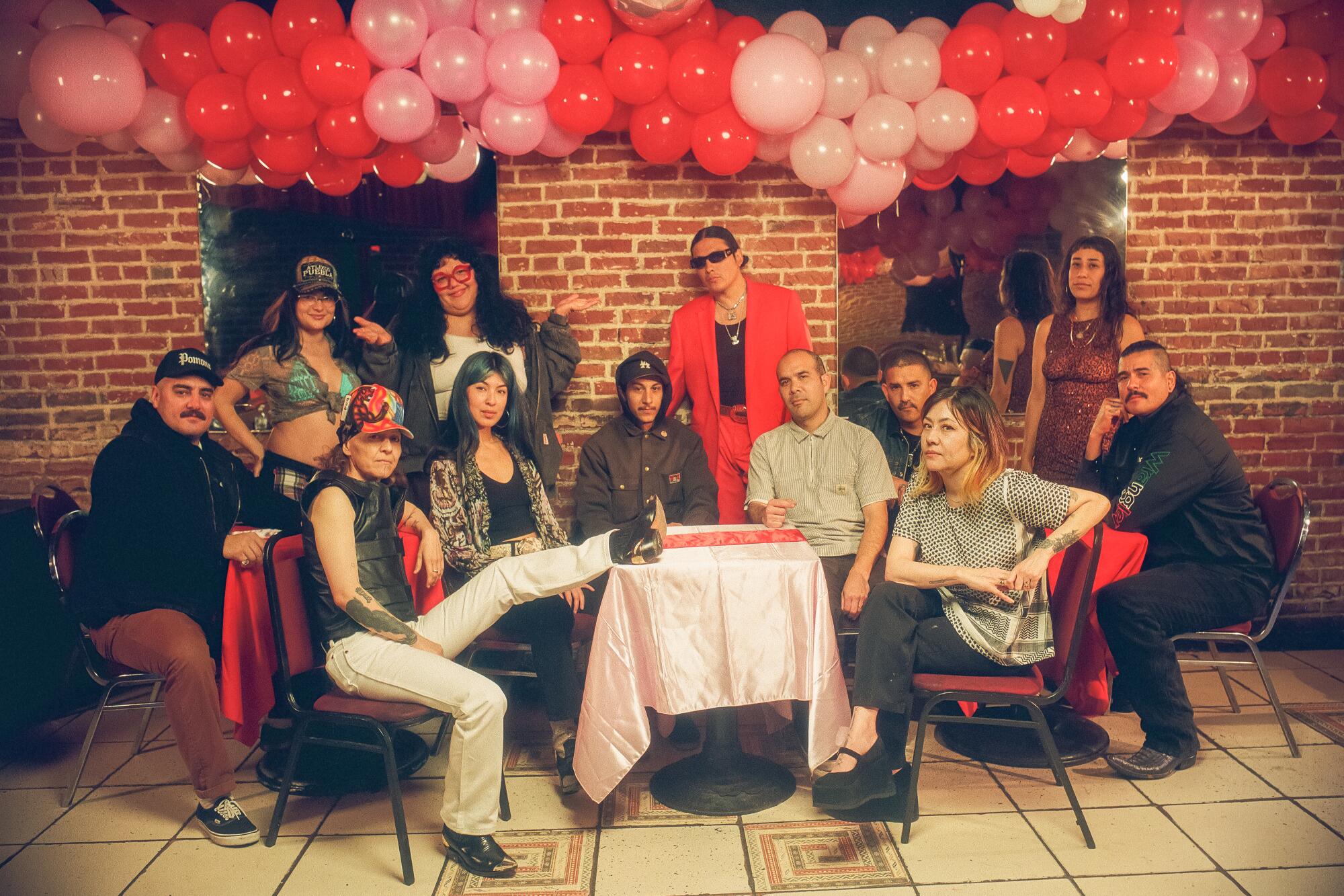 A group of artists gather around tables, pink and red balloons above them.