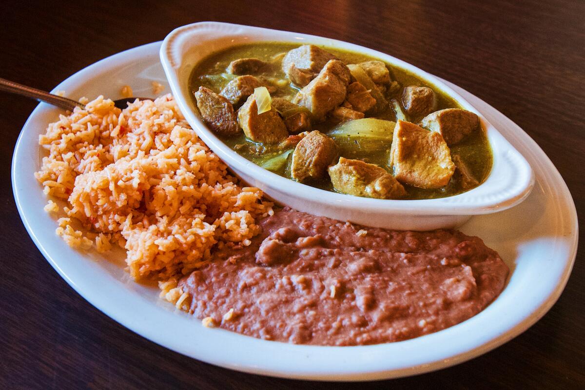 A photo of a ceramic oval bowl of pork in chile verde with a side of rice and beans.