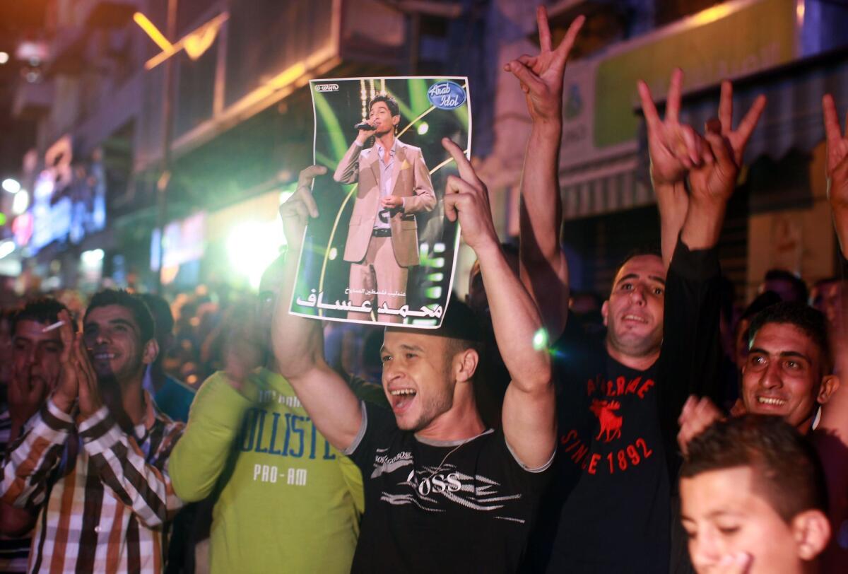 A Palestinian holds a picture of Muhammad Assaf, a Palestinian finalist on the "Arab Idol" talent show, as fans watch his televised performance in the West Bank city of Ramallah.