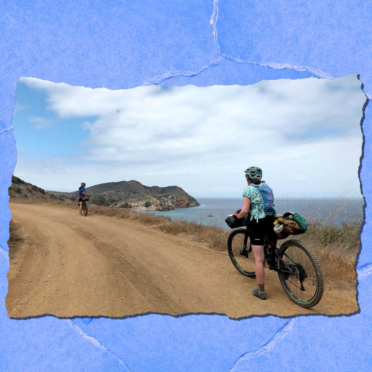 Two people on bikes along a seaside dirt road.