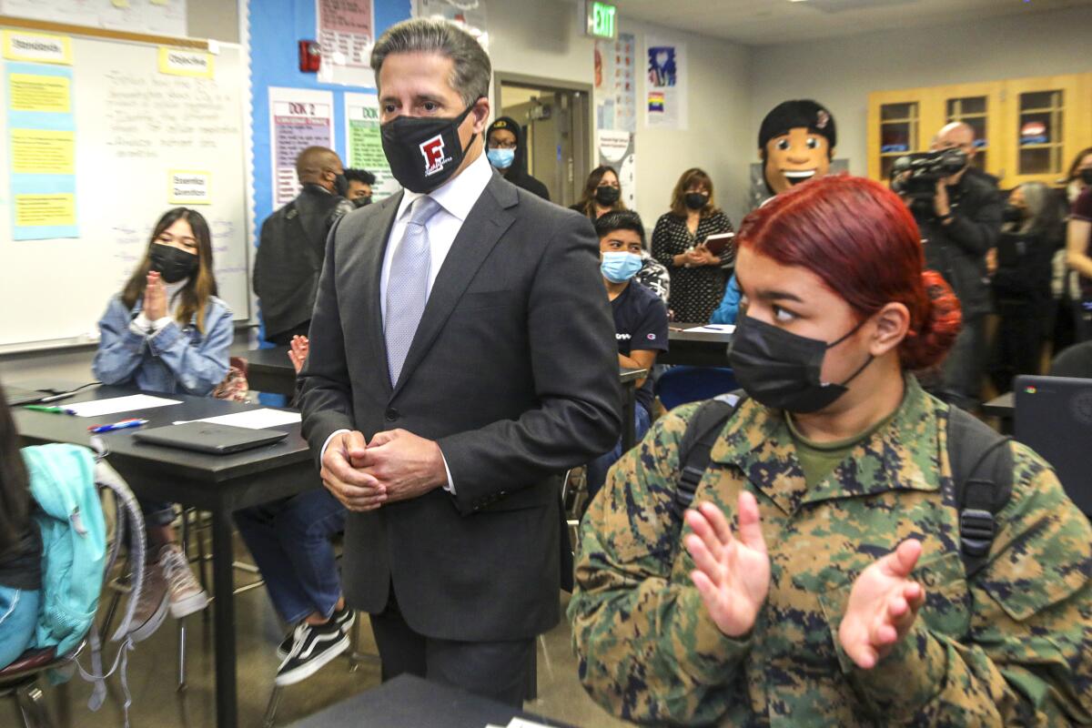 A man in a suit in the middle of a classroom with other people.