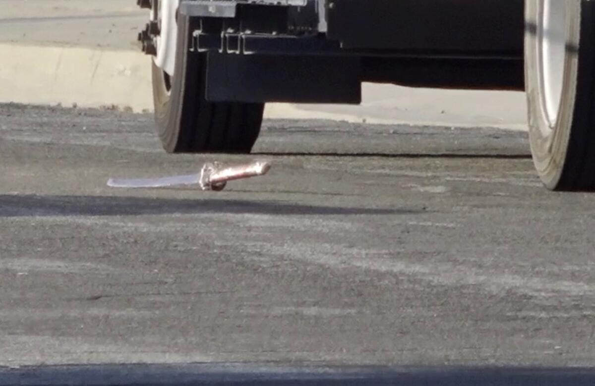 A sword is seen on the pavement next to the wheels of a vehicle