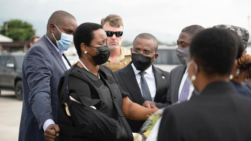 Martine Moise, in a mask, is surrounded by a group of men.