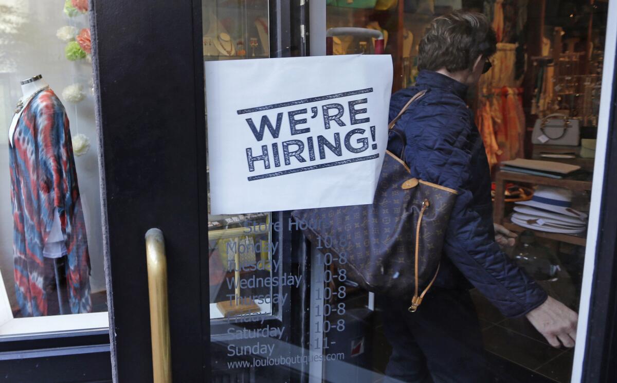A woman passes a "We're Hiring!" sign while entering a clothing store in downtown Boston on May 18.