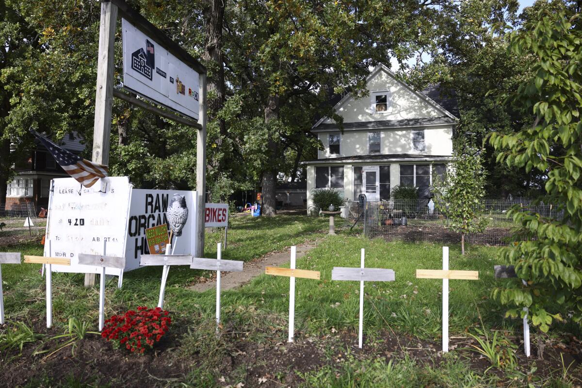 A white home with white crosses in a row on the front lawn and red flowers below one cross