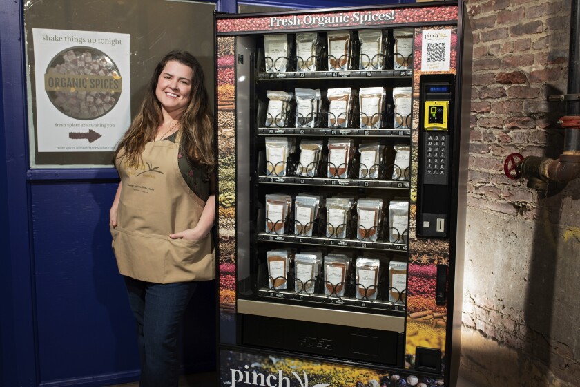 This March 10, 2021 photo shows Meaghan Thomas, co-owner of Pinch Spice Market, with a vending machine the company installed outside its Louisville, Ky. factory to make sales easier during COVID-19. The vending machines helped the company cater to customers as it struggled through the COVID-19 pandemic. It’s now a permanent addition. (Cornetet Fusion Photography/Pinch Spice Market via AP)