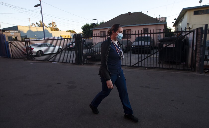 Medical assistant Ana Ivette Zacarias walks to her car in her uniform and a mask.