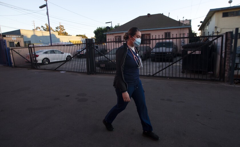 Medical assistant Ana Ivette Zacarias walks to her car in her uniform and a mask.