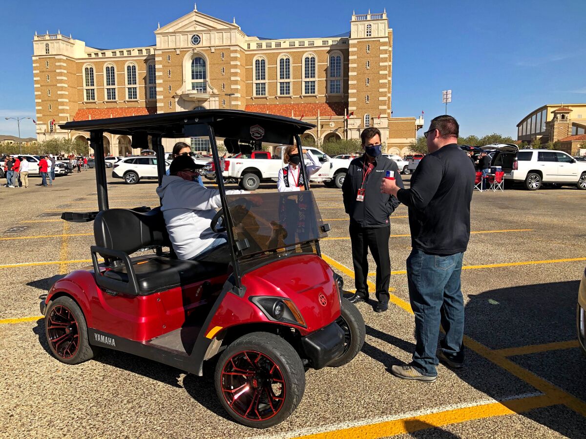 A group of tailgaters talk with a man sitting in a red golf cart