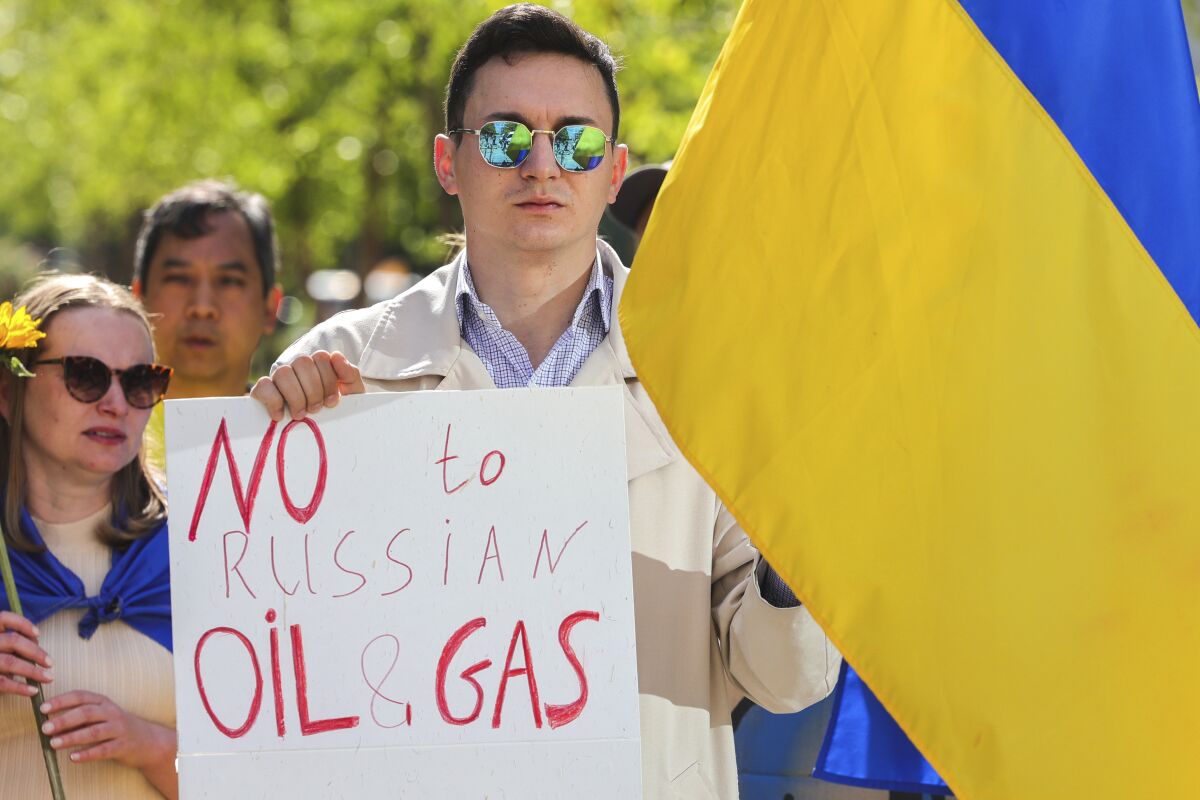 A demonstrator holds a Ukraine flag and a sign reading "No to Russian Oil & Gas."