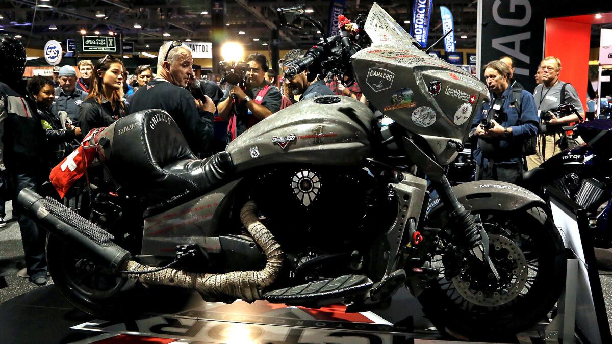 Urs Pedraita, 52, left, talks about his 57,000-mile, six-continent trip in 72 days aboard the Victory Daytona One on display at the Victory exhibit during the Progressive International Motorcycle Show in Long Beach Nov. 18, 2016.