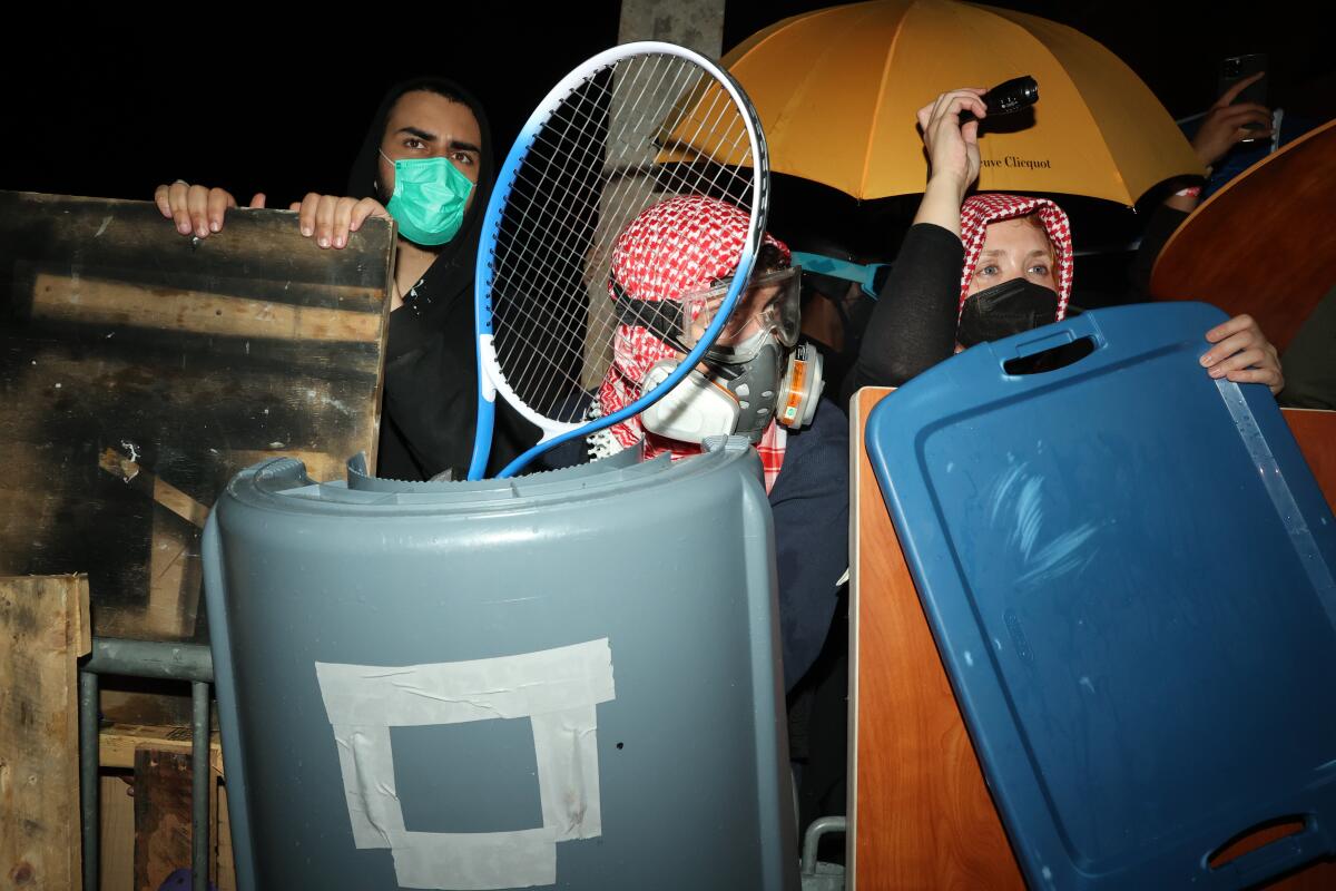 Manifestantes mascarados se amontoam atrás de uma barricada improvisada. 