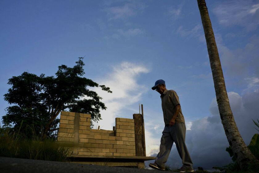 FILE - In this Sept. 8, 2018, file photo, Ramon Alicea Burgos walks past his palm tree, with its top broken off one year ago by Hurricane Maria one outside his partially rebuilt home in the mountain town of Barranquitas, Puerto Rico. A fight between President Donald Trump and Democrats over hurricane relief for Puerto Rico is imperiling a widely backed disaster aid bill that is a top priority for some of Trumps southern GOP allies. (AP Photo/Ramon Espinosa, File)