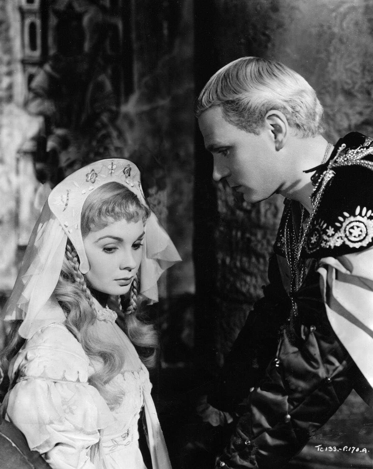 A woman looks down and away from a man, both in Shakespearean costume.