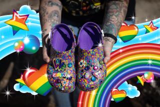 A woman holds rainbow-print Lisa Frank Crocs in her hands.