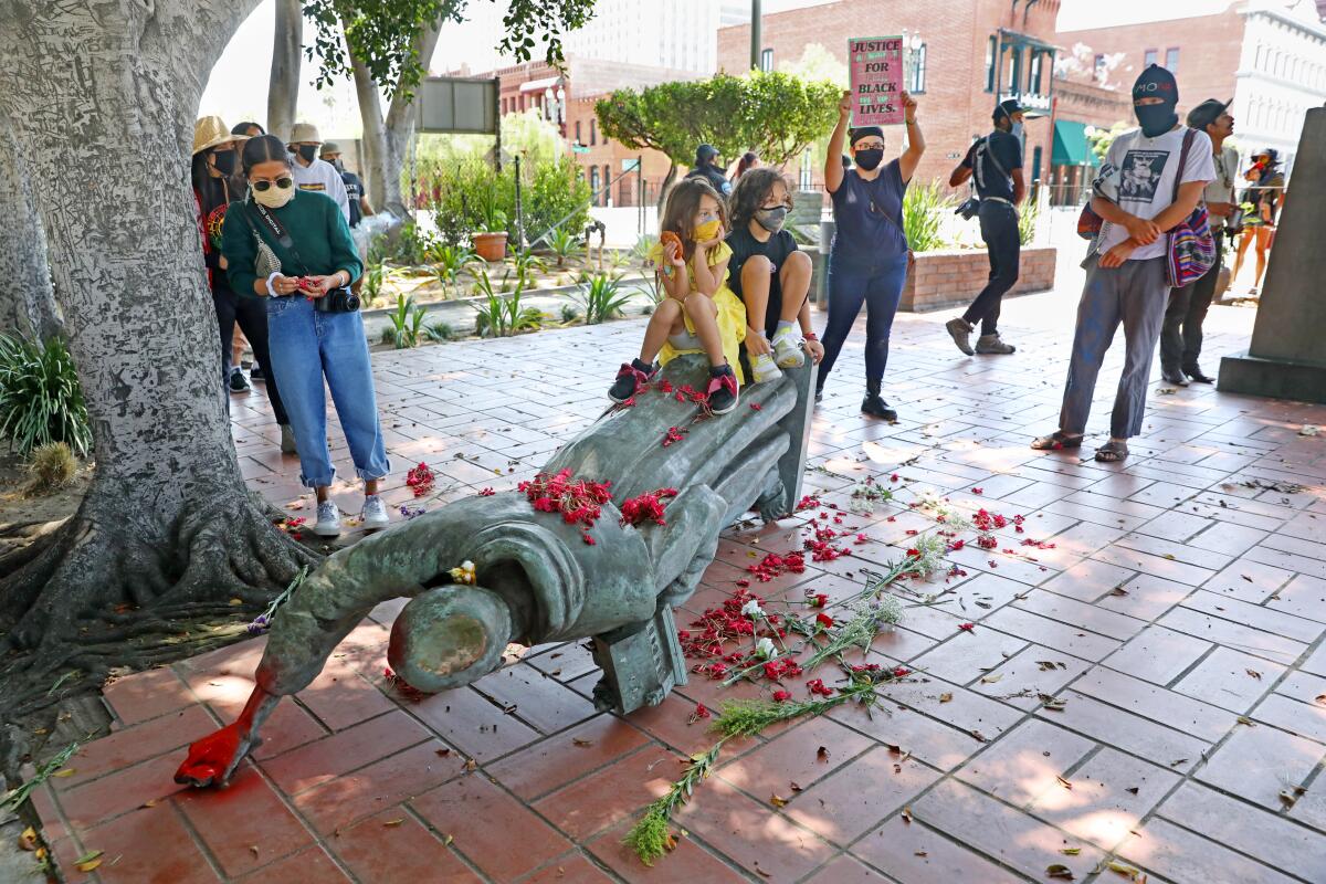 Children pose for pictures on the toppled statue of Junipero Serra