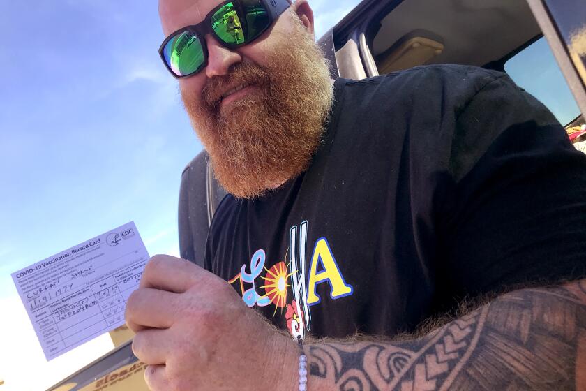 A tattooed and bearded Shane Curran flashes a smile and his vaccine card after receiving his Johnson & Johnson vaccine