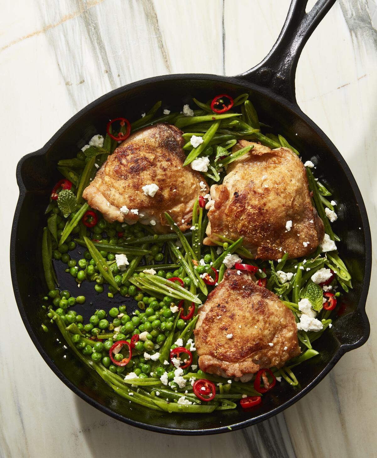 A cast-iron skillet with three chicken thighs over a bed of peas