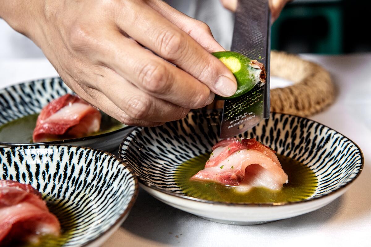 Close-up of a person's hands as they grate lime peel atop chunks of fish in several small dishes.