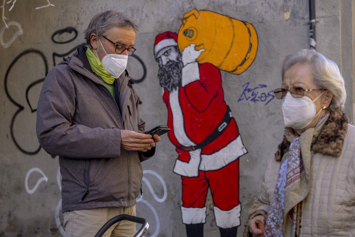 FILE - A man and woman wearing FFP2 masks to curb the spread of COVID-19 are seen in front of a mural depicting Santa Claus, in Madrid, Spain, on Jan. 12, 2022. Spain will end a mandate to wear masks outdoors next week, reverting a late December order against an unprecedented surge of coronavirus infections fueled by a highly contagious mutation. (AP Photo/Manu Fernandez, File)