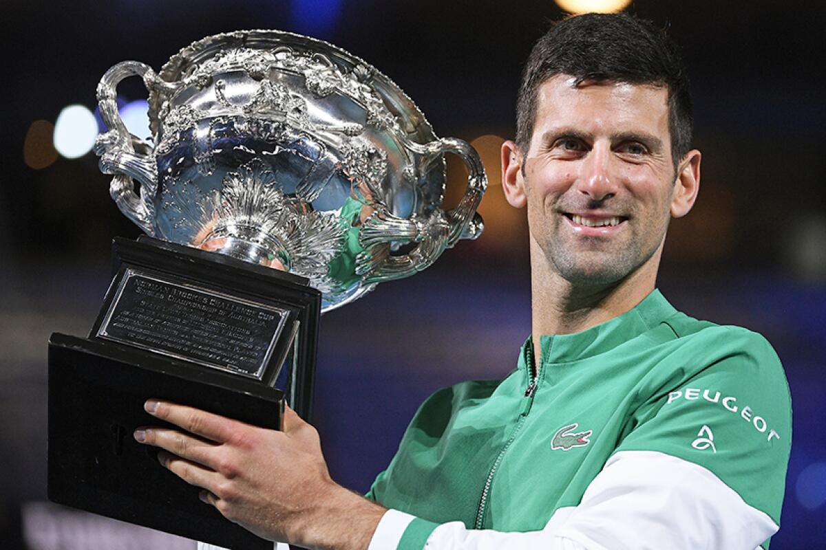 Novak Djokovic smiles and holds up a trophy.