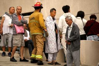 LOS ANGELES, CA - SEPTEMBER 13, 2024 - Wei Xiong Liang, 62, center, his son Andy Liang, 18, white hoody-back to camera, and other residents stand outside their fire damaged apartment along 800 N. Bunker Hill Ave. in Chinatown on September 13, 2024. The fire started at a vacant three-story apartment building under construction and spread to nearby apartment buildings. Around 30 apartment tenants are displaced by the fire. According to L.A.F.D. Captain and Pio Adam VanGerpen, one person is in critical condition after being rescued from the raging fire and two firefighters suffered injuries. 130 firefighters battled the blaze which started at 3:34 a.m. The apartment building and the 3 story building where the fire started were red tagged. (Genaro Molina/Los Angeles Times)