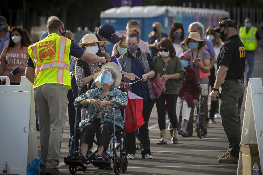 Anaheim, CA - January 13: Officials take the temperature of Orange County active Phase 1A (critical and healthcare workers) residents as they line up to enter large tents at Orange County's first large-scale vaccination site to receive the Moderna COVID-19 vaccine in the Toy Story parking lot at the Disneyland Resort in Anaheim Wednesday, Jan. 13, 2021. Orange County supervisors and Orange County Health Care Agency Director Dr. Clayton Chau held a news conference discussing the county's first Super POD (point-of-dispensing) site for COVID-19 vaccine distribution. The vaccinations are at Tier 1A for people who have reservations on a website. The site is able to handle 7,000 immunizations per day. Their goal is to immunize everyone in Orange County who chooses to do so by July 4th. (Allen J. Schaben / Los Angeles Times)