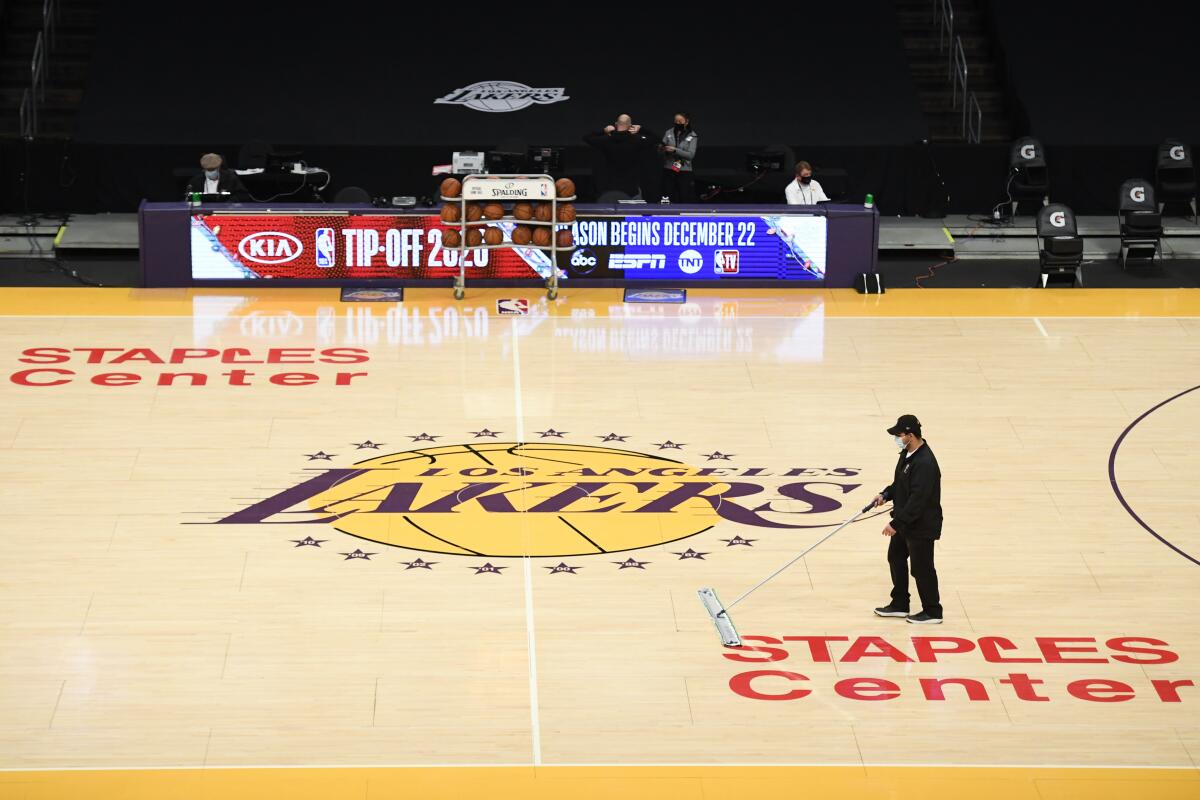 A Staples Center staff member with a mask cleans the floor before a preseason game between the Clippers and Lakers.