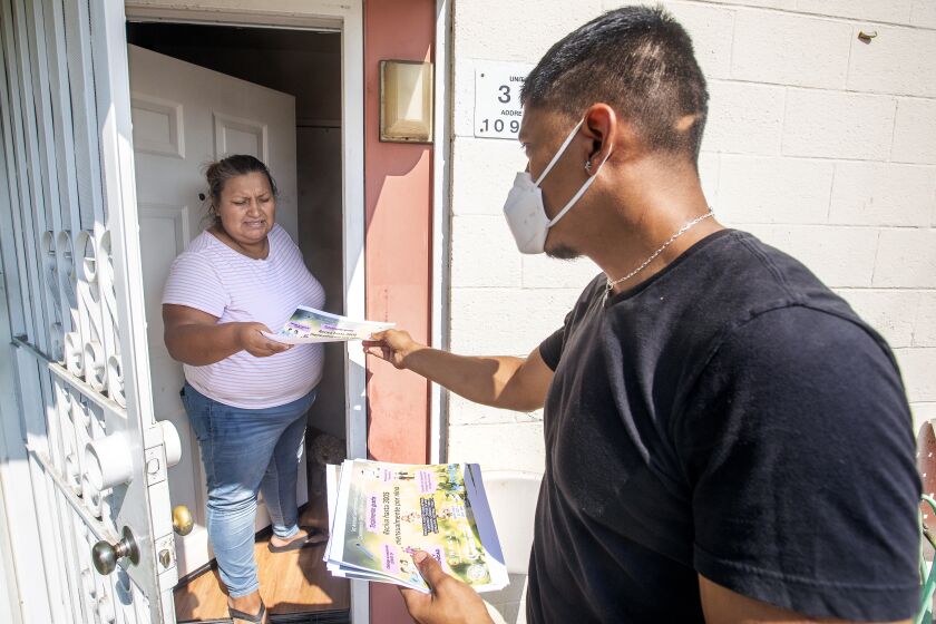 PACOIMA, CA - AUGUST 25, 2021: San Fernando Gardens resident Gloria Acosta, 38, receives a flyer from Adrian Ramirez, a volunteer for Ground Game L.A., letting her know about an event that day to spread information about the child tax credit, provide vaccinations, and offer immigration and tax help. (Mel Melcon / Los Angeles Times)